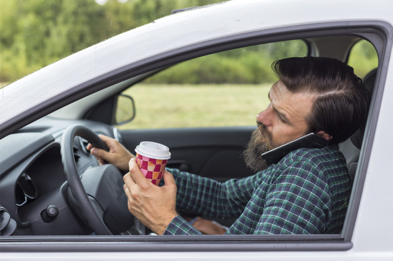 A man driving while on the phone and holding a cup of coffee. Learn about the risks of multitasking.