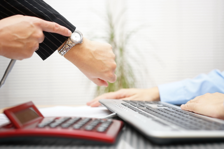 A boss pointing at their watch in front of an employee. Learn about how to discipline employees who have experienced work injuries.