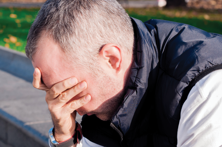 A stressed man with his hand over his face. Read about preventing stress among employees.