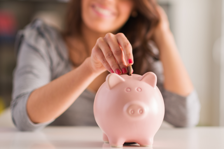 A person putting a coin into a piggy bank. Learn about tips to lower your work comp costs.