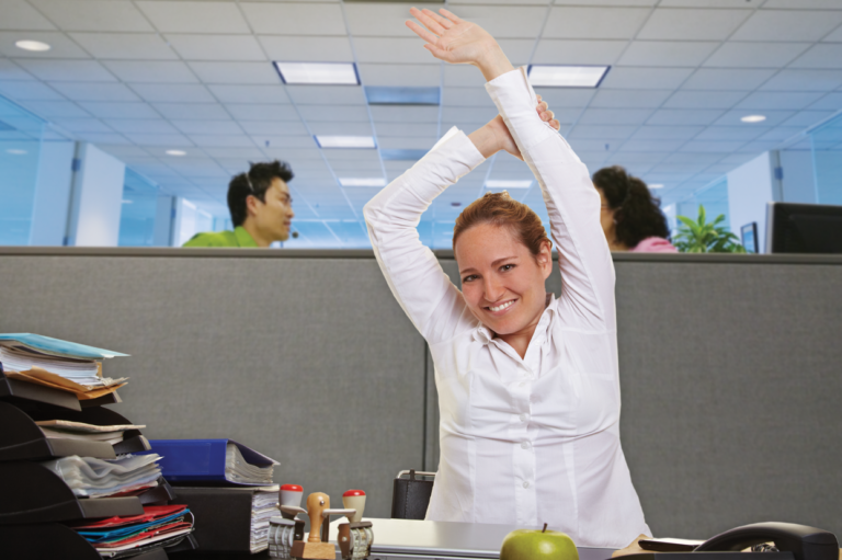 A woman stretching at her desk. Read about how to boost workplace safety efforts by connecting wellness.