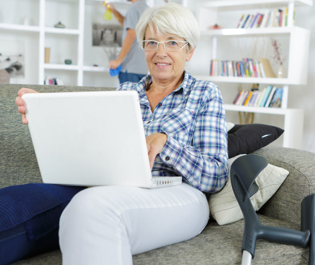 Woman with injured leg sitting at home and looking at a laptop computer